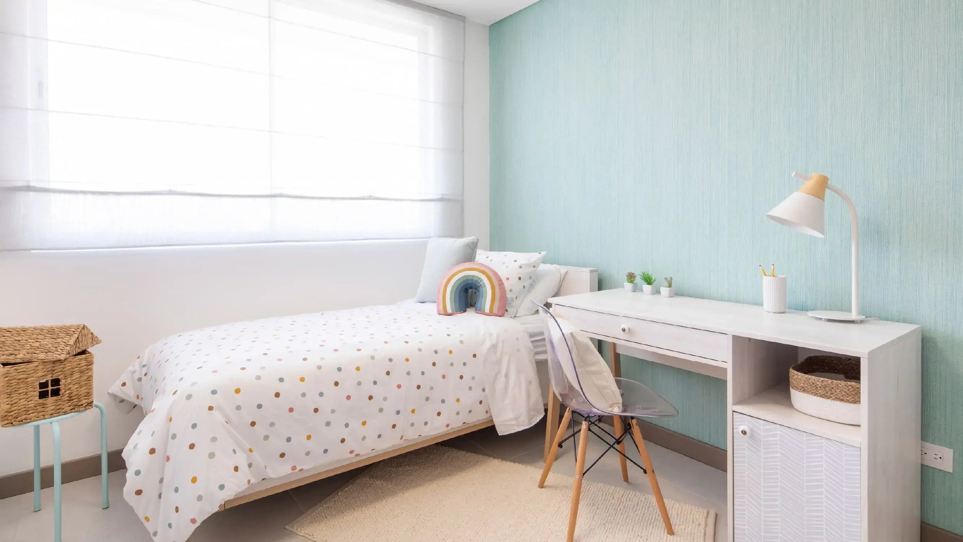 Render de habitación infantil en la casa modelo de Palermo Homes, Heredia. Muestra cama individual con ropa de puntos y cojín de arcoíris, escritorio de estudio blanco con silla transparente y ventanal con persiana romana.