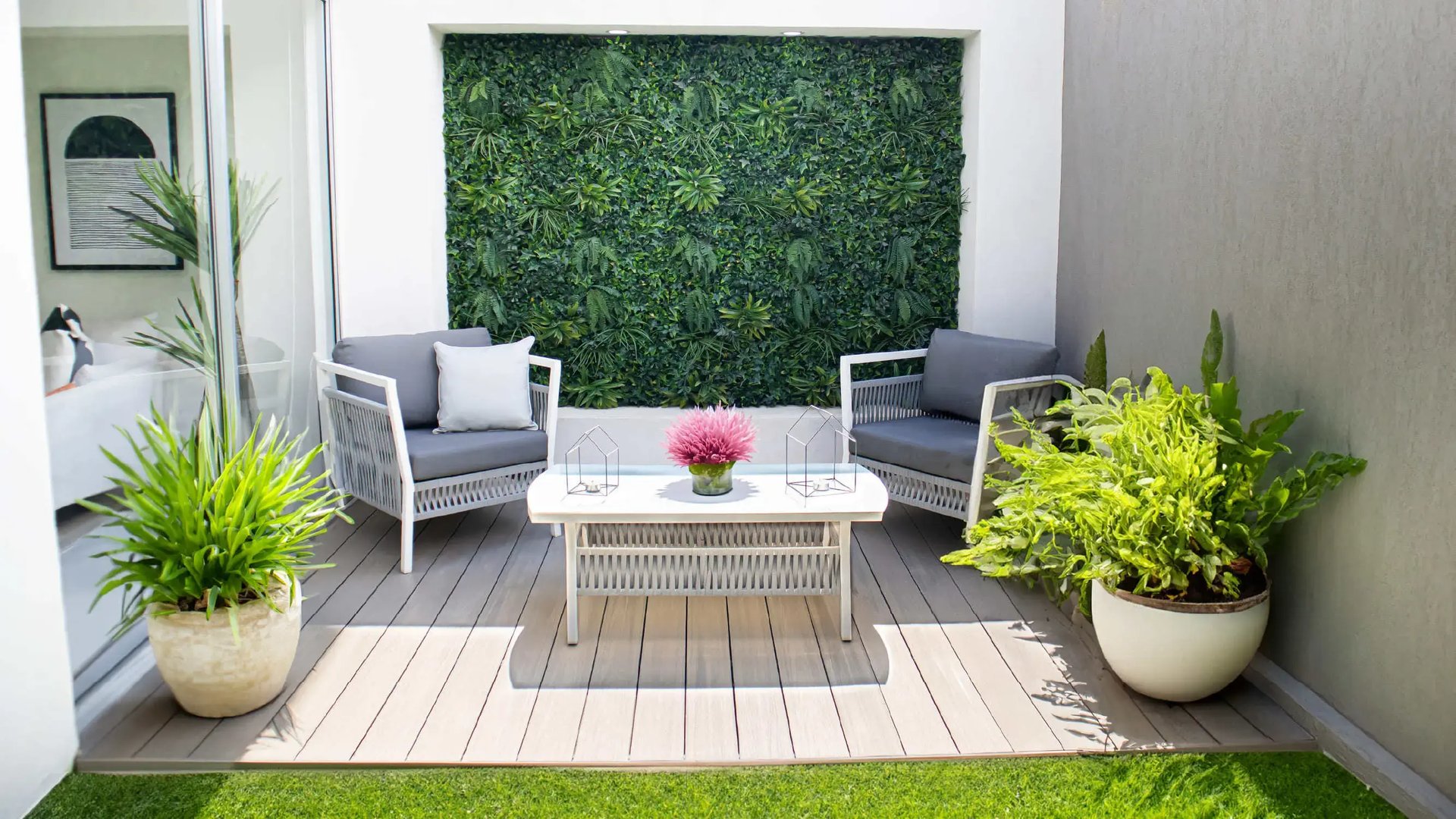 Render de terraza interior en Palermo Homes, Heredia. Presenta un patio de luz con piso deck, modernos muebles de exterior grises, mesa de centro, un denso jardín vertical en la pared y una puerta corrediza de vidrio que conecta con la casa.