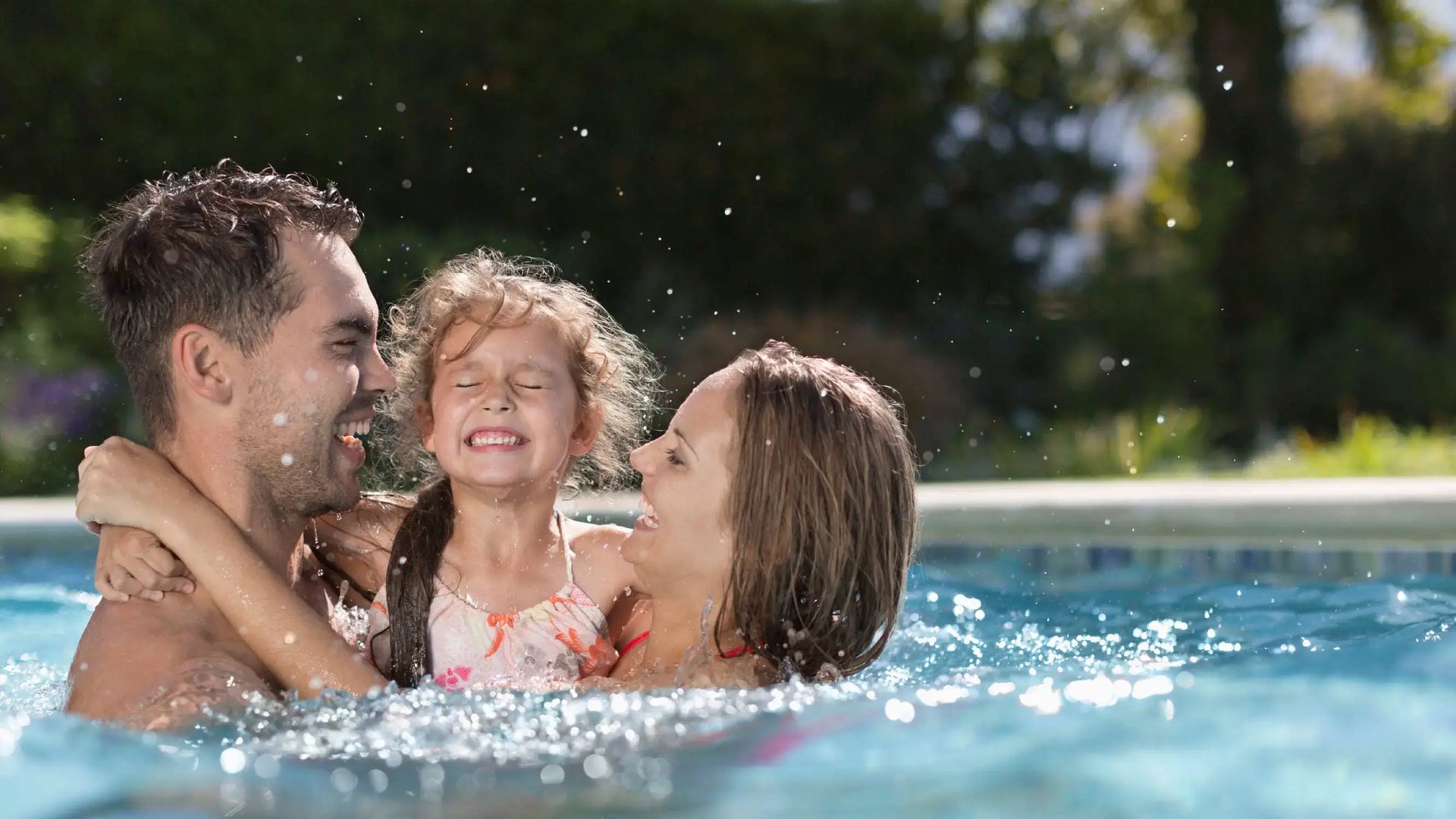 Familia disfrutando y salpicando agua en la piscina recreativa de Palermo Homes, Heredia. Muestra a padres e hija sonriendo en un día soleado.