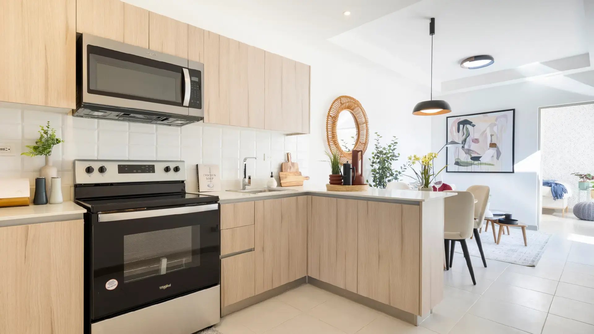 Cocina moderna de concepto abierto en Condominio Naz, Alajuela. Muestra muebles de melamina clara, electrodomésticos de acero inoxidable, desayunador y vista integrada hacia el comedor y la sala decorada.