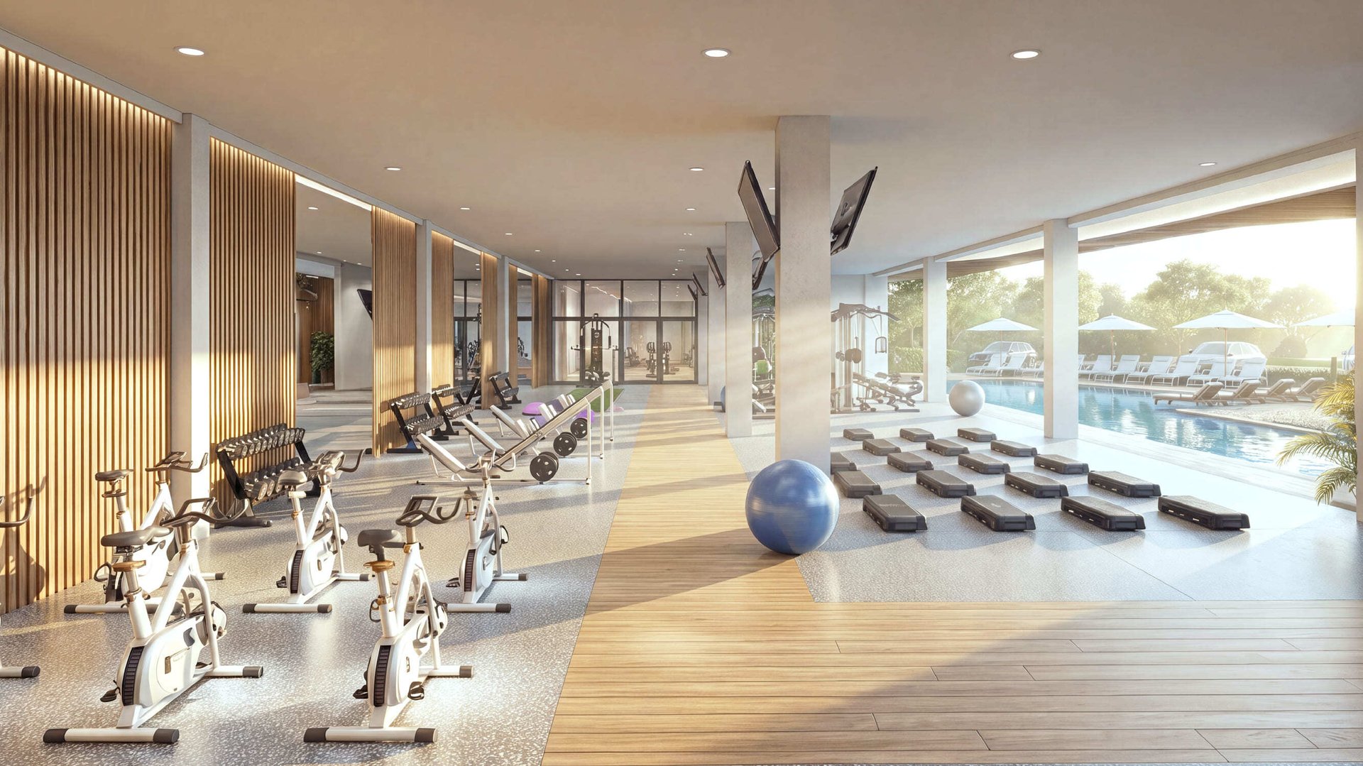 Gimnasio residencial moderno equipado con bicicletas estáticas de spinning, pesas, escalones para ejercicio y pelota de fitness, con amplios ventanales y vista directa a una alberca exterior con camastros.