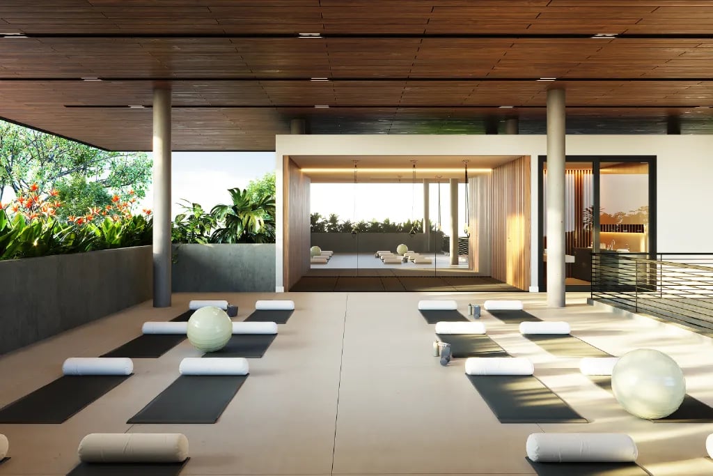 Render de un estudio de yoga moderno y al aire libre. Muestra tapetes negros ordenados con almohadones blancos, pelotas de ejercicio, cielorraso de madera e iluminación cálida, con vistas a un jardín tropical.