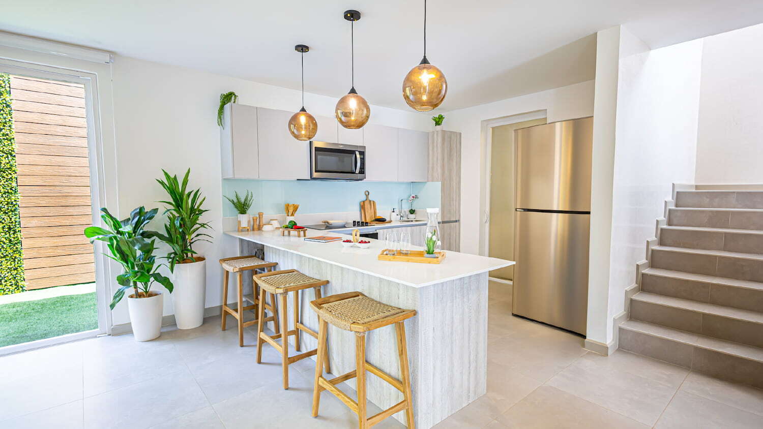 Cocina moderna con isla y desayunador de concepto abierto en Condominio Nasara, con tres lámparas colgantes, refrigerador de acero inoxidable y escaleras a la derecha.