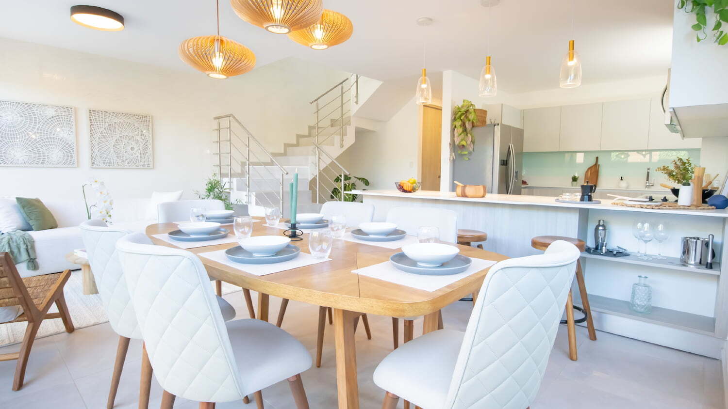 Amplio comedor de concepto abierto con mesa de madera y sillas blancas modernas, integrado con la cocina y una escalera al fondo en Condominio Nasara.
