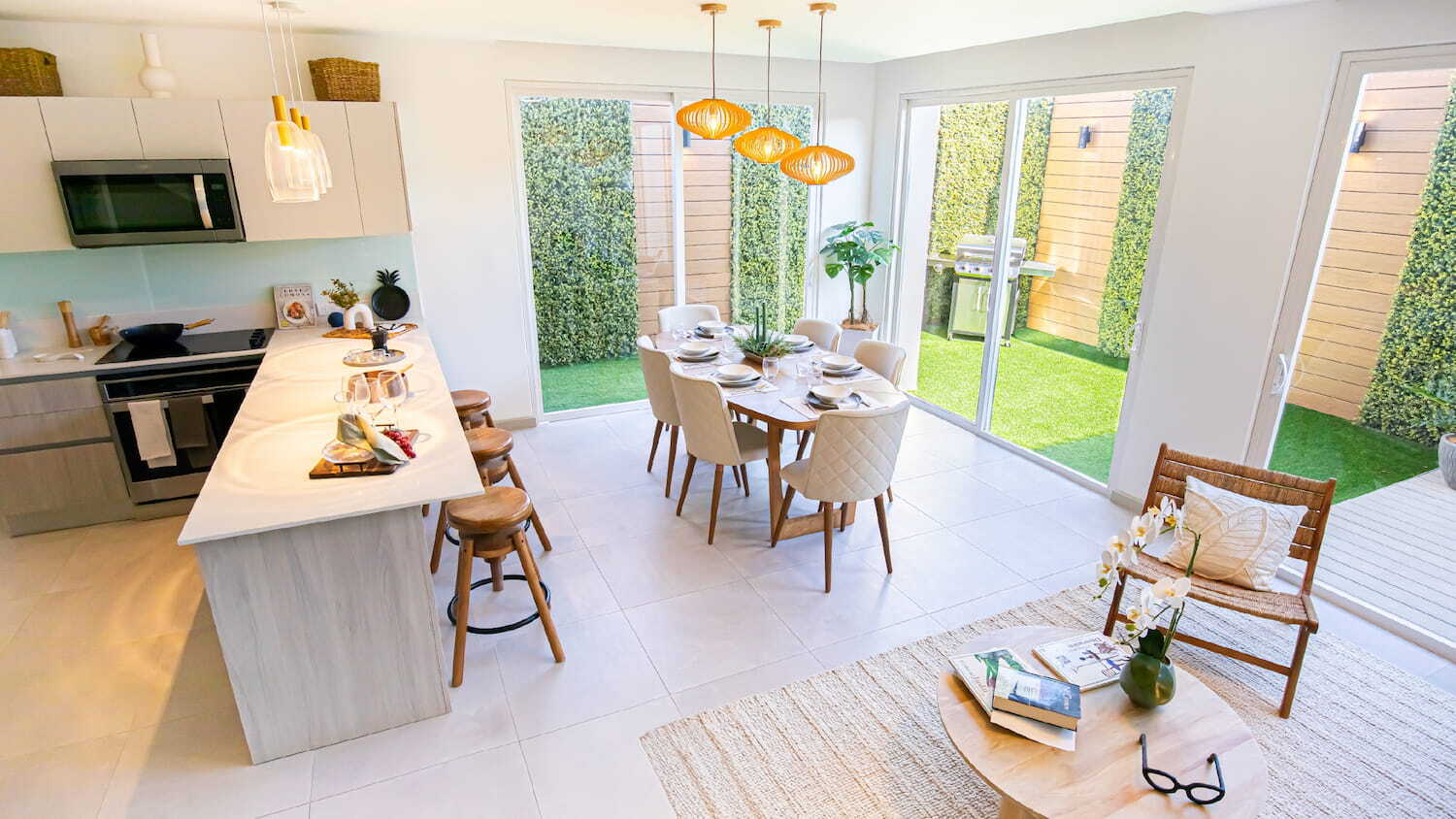 Vista amplia del diseño de interiores de concepto abierto en Condominio Nasara, mostrando la cocina moderna con isla, un comedor iluminado por lámparas colgantes y grandes ventanales con acceso al jardín.