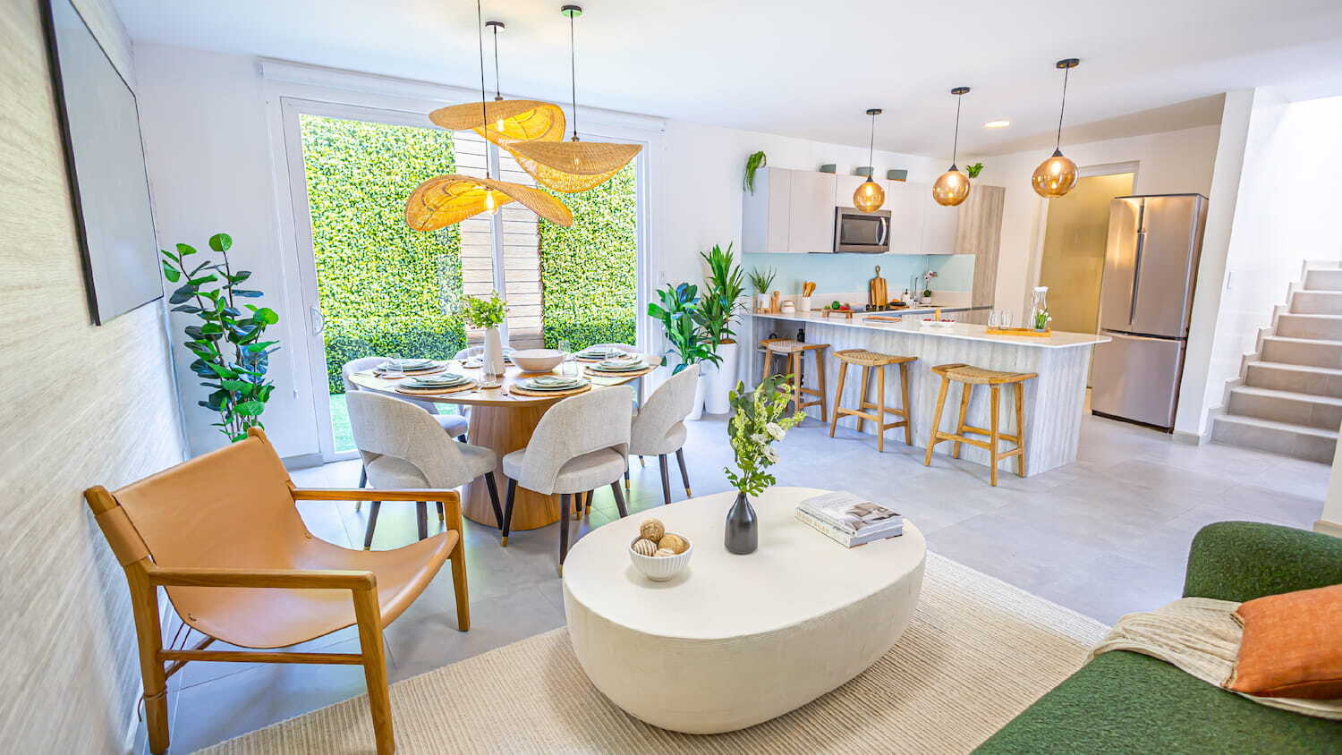 Vista amplia del diseño interior en Condominio Nasara que muestra la sala de estar, un comedor iluminado con lámparas tejidas y una cocina de concepto abierto con barra.