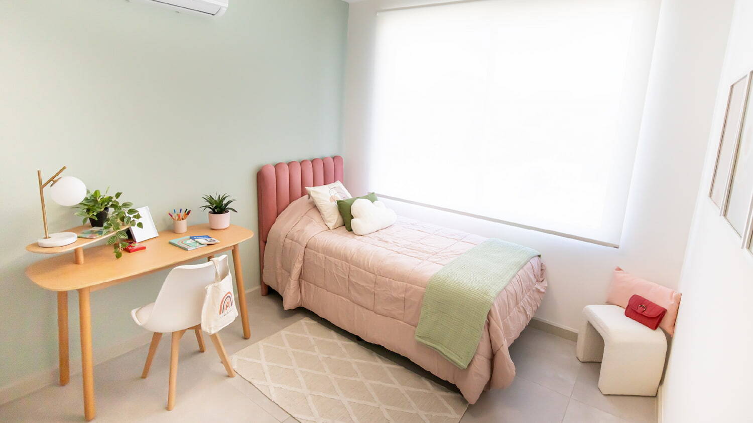 Habitación juvenil moderna en Condominio Nasara con una cama individual de cabecera rosa, un escritorio de madera con silla blanca y una ventana grande iluminada.