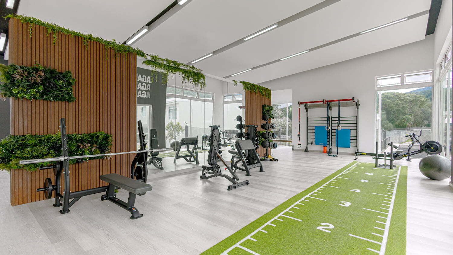 Gimnasio moderno y equipado en Condominio Nasara con área de pesas, espejos, carril de césped artificial para entrenamiento funcional y ventanales iluminados.