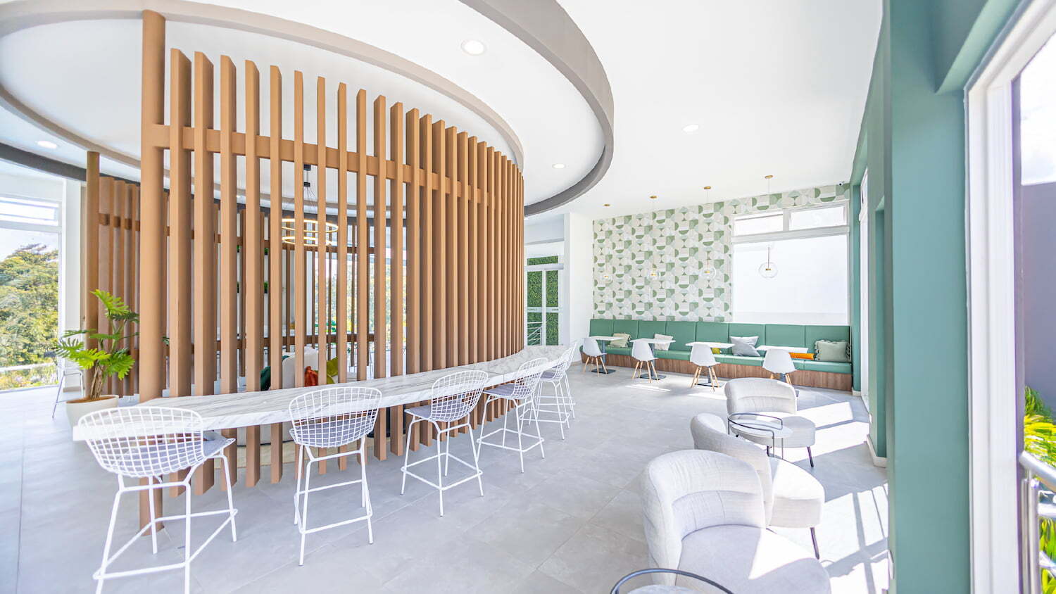 Interior de la casa club de diseño moderno en Condominio Nasara, con una barra curva de mármol, taburetes altos, sillones cómodos y una zona de cafetería al fondo con asientos verdes.