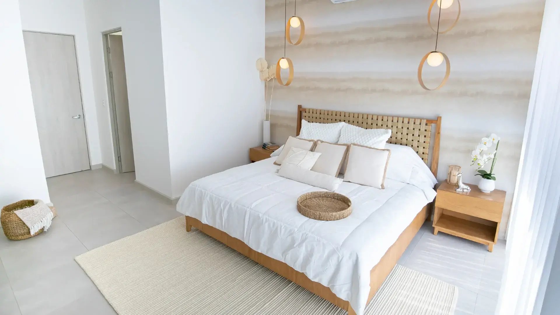 Imagen del dormitorio principal en Condominio Nasara, Santa Ana. Presenta una cama queen con cabecera de mimbre, lámparas colgantes de diseño, pared decorativa con textura y accesos privados a un walk-in closet y baño en-suite.