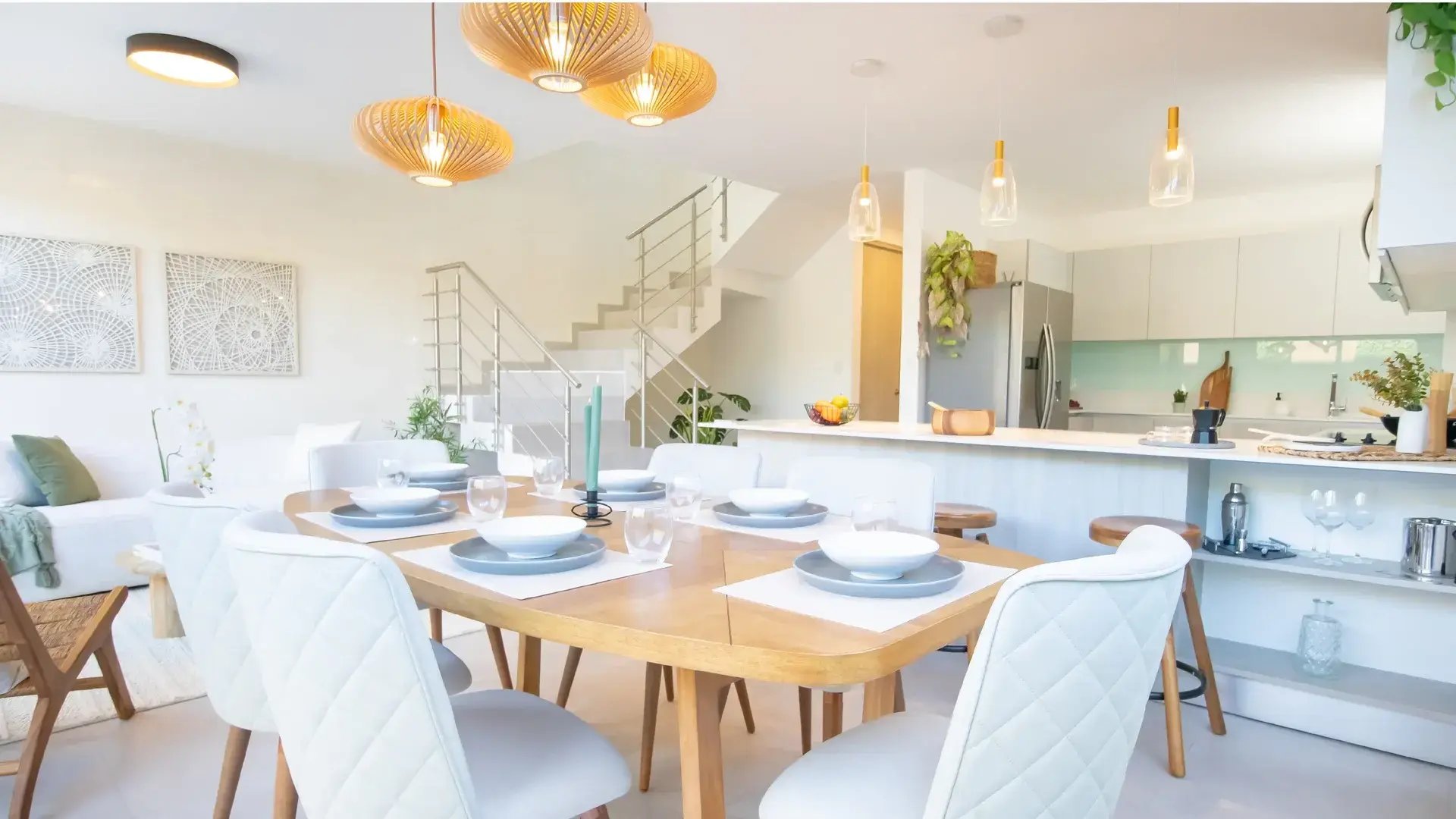 Interior de casa en Condominio Nasara, Santa Ana. Muestra comedor moderno con lámparas de diseño, cocina con desayunador de sobre blanco y escaleras con barandales de acero inoxidable.