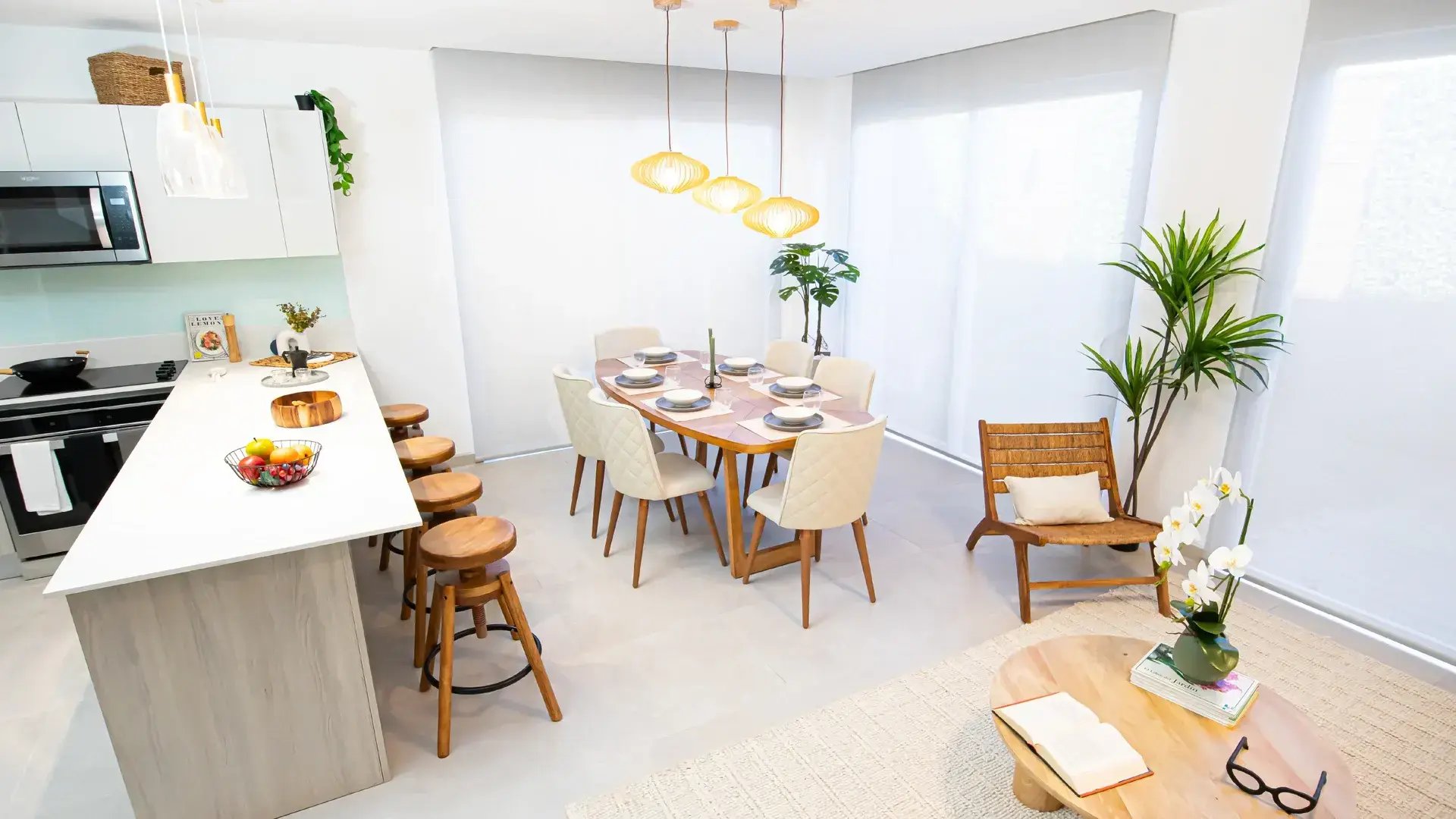 Vista de planta abierta en Condominio Nasara, Santa Ana. Muestra cocina moderna con sobres blancos, desayunador con bancos de madera, comedor para seis personas y sala iluminada con grandes ventanales.