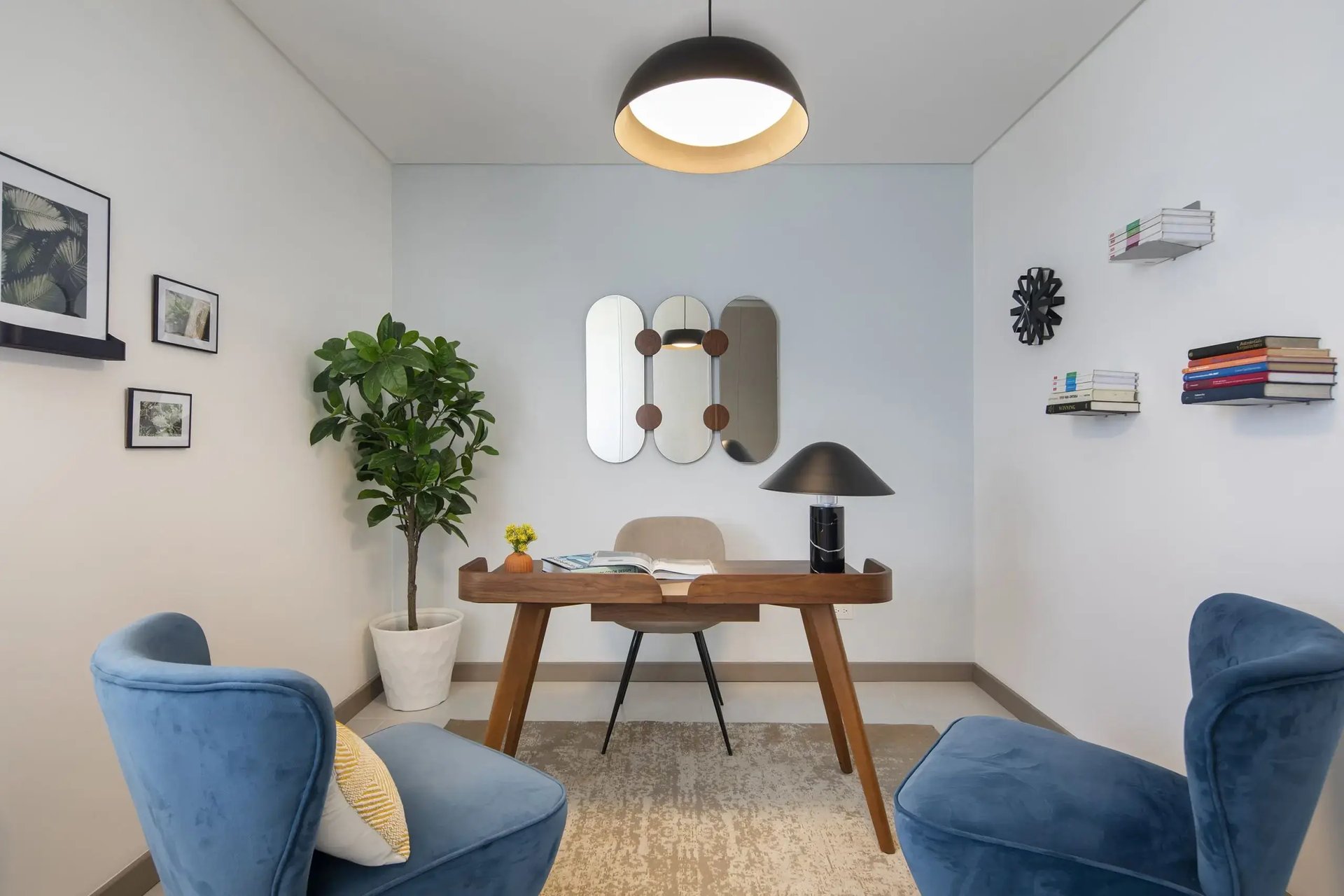 Interior de oficina privada en Condominio Blue, Cariari. Muestra un escritorio de madera de diseño moderno, silla ergonómica, butacas de terciopelo azul, estantería minimalista y decoración contemporánea en tonos neutros.