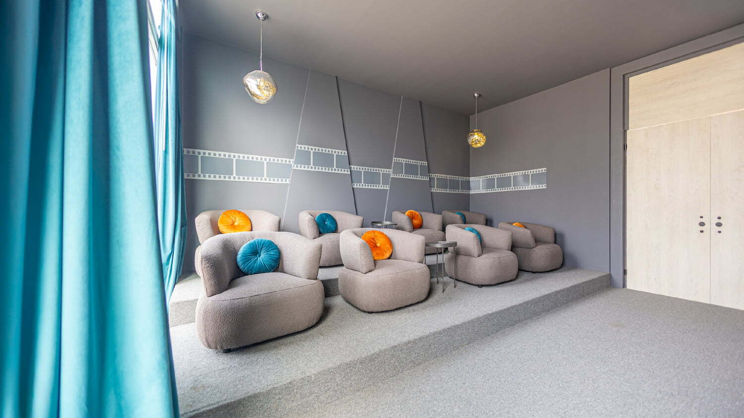 Sala de cine o home theater en las amenidades de Condominio Nasara con sillones acolchados en plataformas escalonadas, cojines de colores y detalles de rollos de película en la pared.