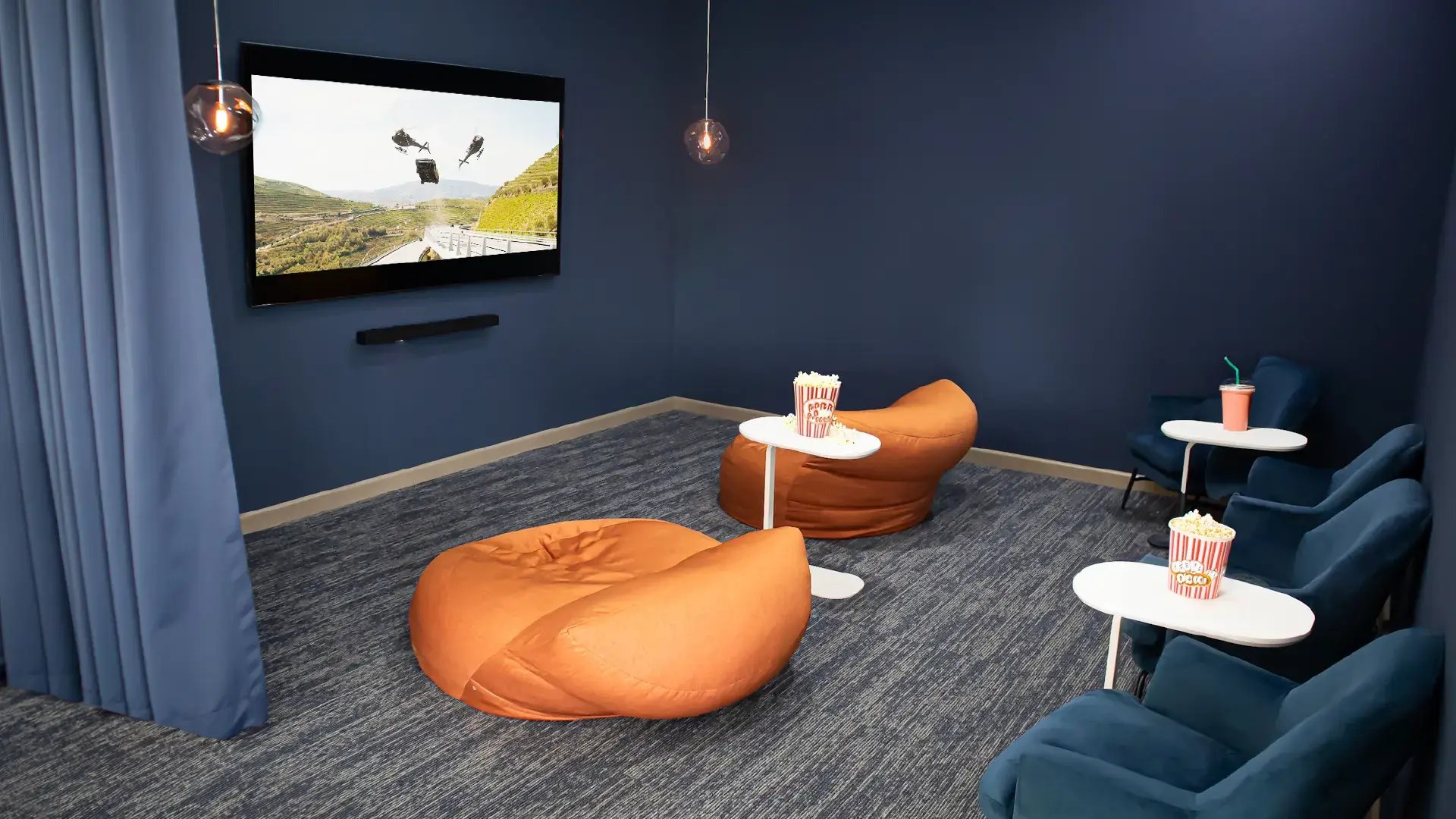 Sala de juegos y área de cine en Condominio Blue, Cariari. Muestra una pantalla grande, sillones tipo bean bag color naranja, butacas azules y mesas pequeñas con palomitas, en un ambiente moderno y relajado.