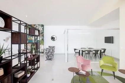 Sala moderna con estantería abierta sillones de colores y comedor con mesa y sillas al fondo