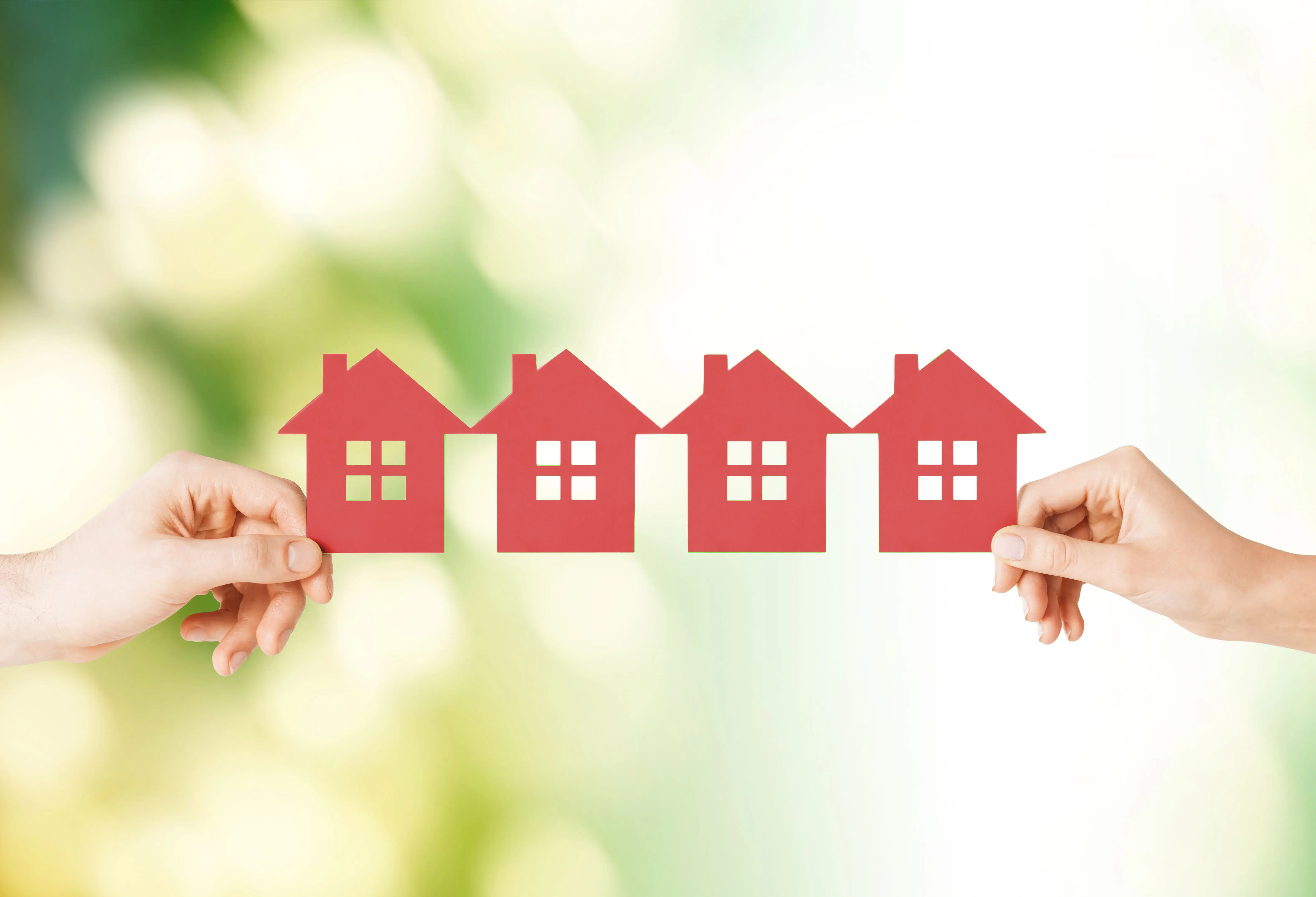 Manos sosteniendo figuras de casas rojas alineadas representando viviendas o propiedades